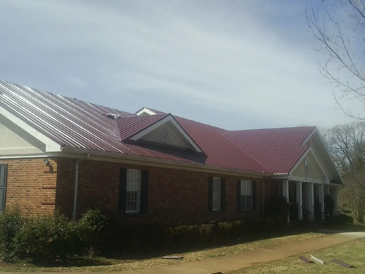 Red metal roof with gabled entries on a long brick building, from a Hail Damage Roof Repair job in Jensen Beach