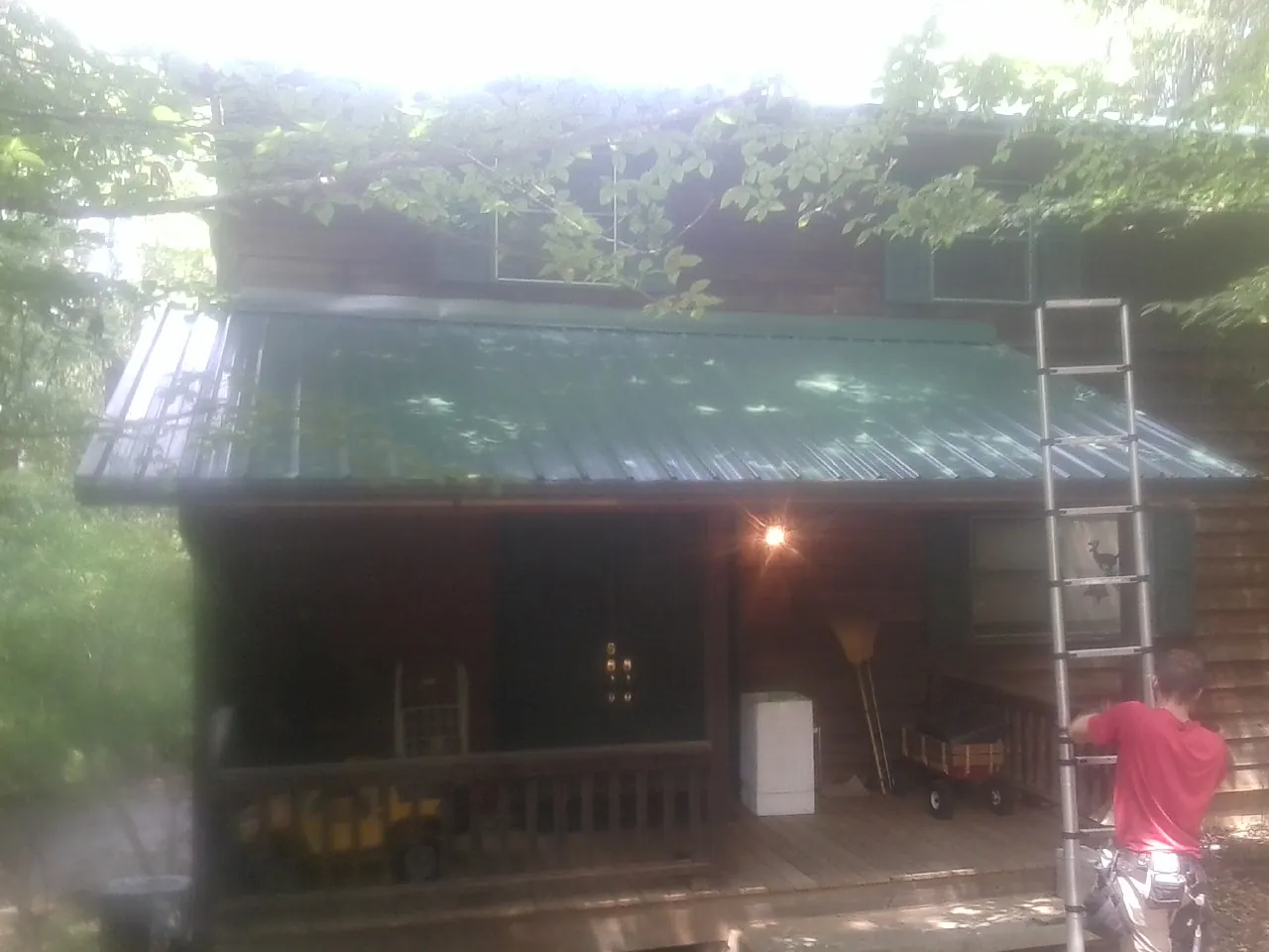 Worker on a ladder at the green porch roof of a wooded cabin in Jensen Beach