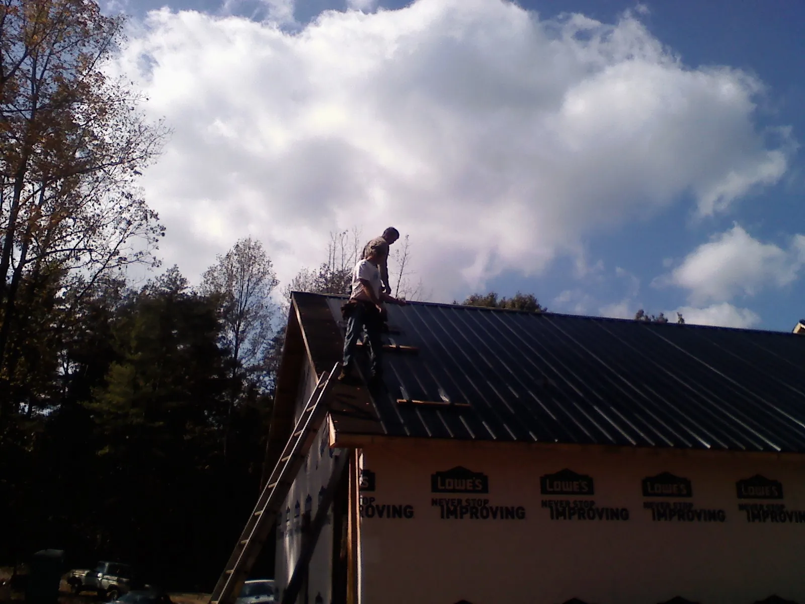 Roofer fastening dark metal panels high against a cloudy sky, from a Roof Inspection job in Jensen Beach