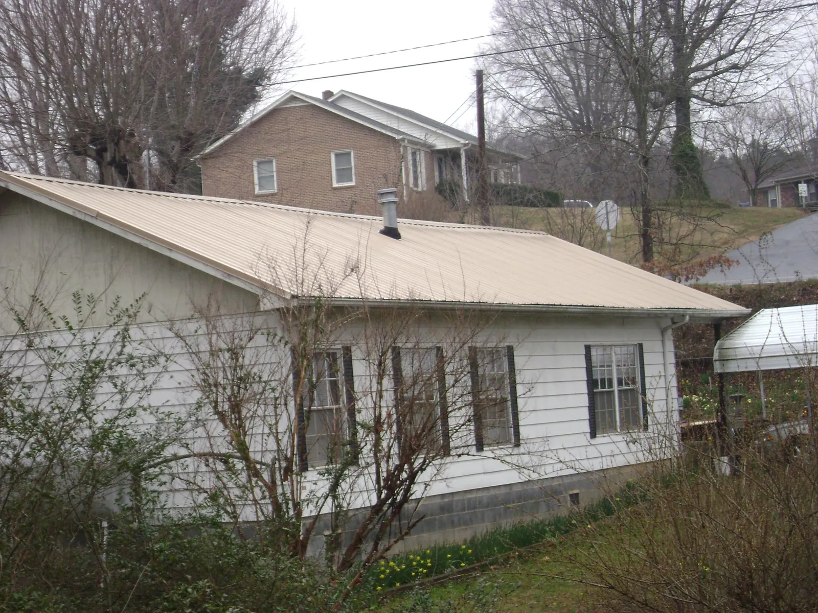 Tan metal roof on a white sided house set into a hillside — Commercial Roofing by Roofing Brothers in Jensen Beach